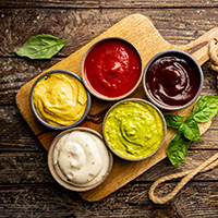 Set of different bowls of various dip sauces on wooden background, top view